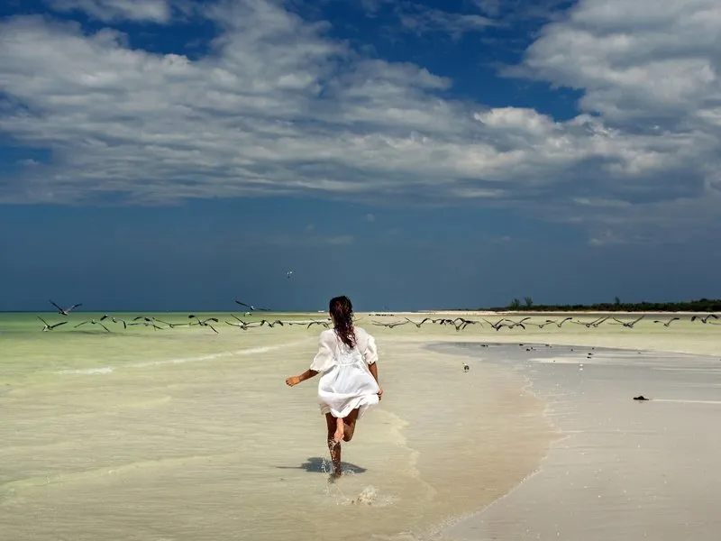 Ženska teče po beli peščeni plaži otoka Holbox pred hotelom